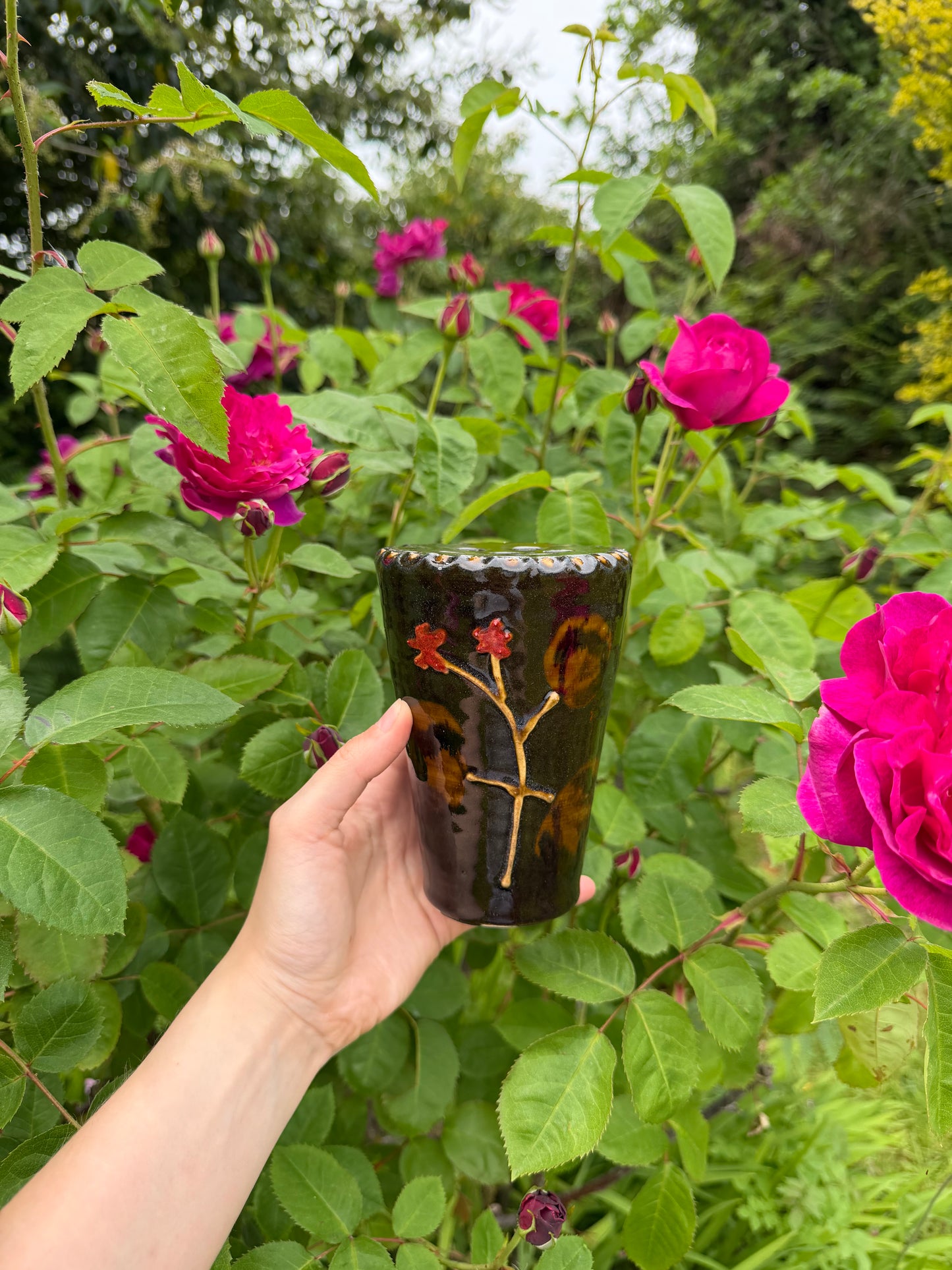 Hand holding a decorative vase with pink roses in the background