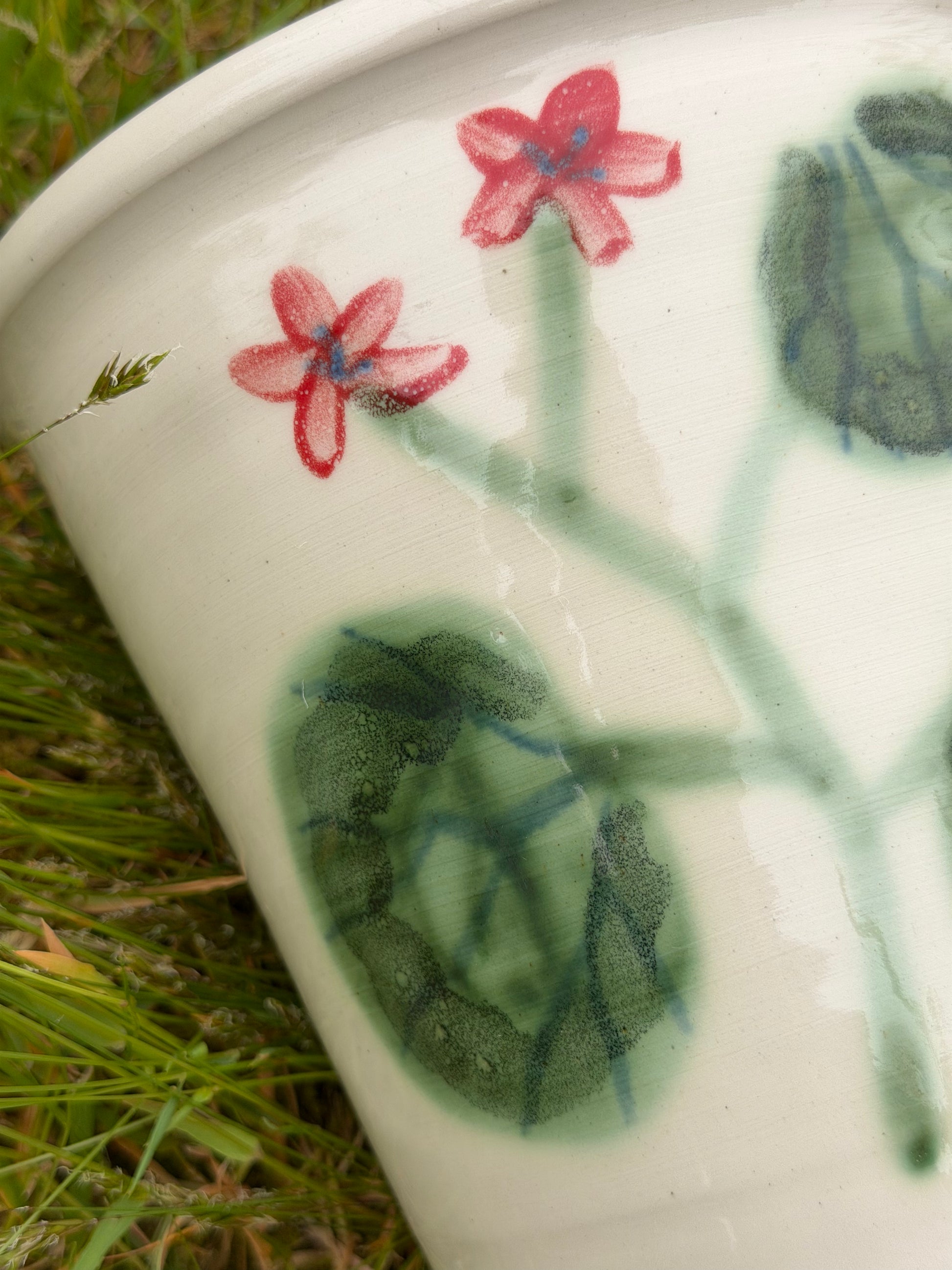 Ceramic cup with floral and leaf design on grass