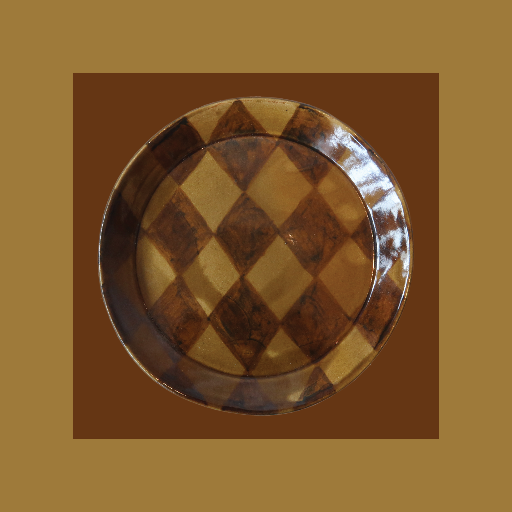 Stoneware plate, formed on a mould and painted by hand.  Fired once to 1000 degrees celsius, then signed, waxed, and dipped into a homemade glossy honey glaze. A harlequin pattern is painted by hand on top of the glaze. Once dry the piece is ready for its final 1230 degree firing.  Approximately:   19cm diameter    Paige Mitchell, Handmade Ceramics.